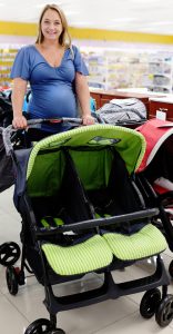 A very pregnant woman smiles beautifully as she chooses a double pushchair, designed for twins, in a specialist baby shop.