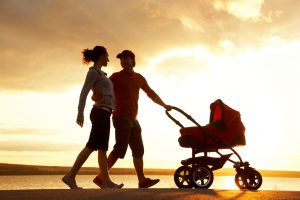 Silhouettes of happy parents walking with stroller on the seacoast