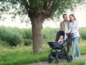 Portrait of a smiling young family walking outdoors and pushing baby in pram