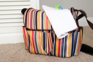 A diaper bag is packed and ready to go, with a burping cloth draped on top of it.