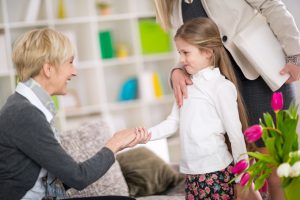 Little girl introduction her new babysitter, girl timidly shake hands with mature woman