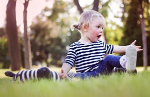 Beautiful happy little baby girl sitting and talking with herself on a green meadow on the nature in the park
