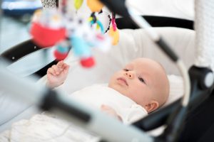 Cute little baby boy lying in a stroller and playing with toys. He is focused on toys above him.