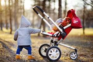 Toddler boy playing with his stroller walking outdoors at the warm spring day