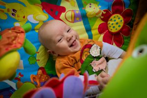Excited happy smiling small three months old baby boy playing in colorful playpen. Selective focus on the baby. Heavy vignette.